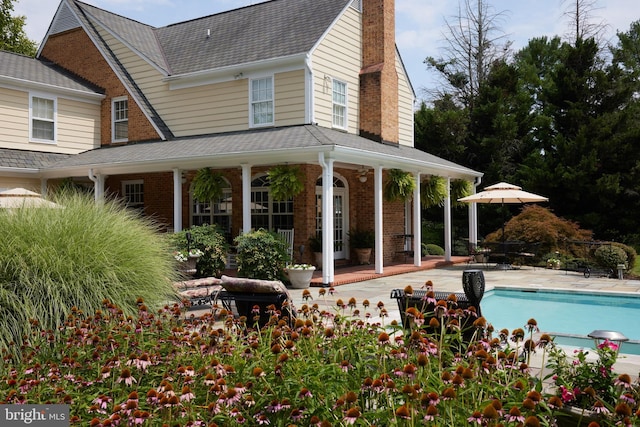 rear view of house featuring an outdoor pool, a patio area, a chimney, and brick siding