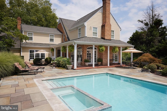 back of property with a chimney, a patio area, brick siding, and a pool with connected hot tub