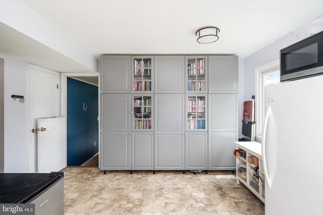 interior space with freestanding refrigerator, stainless steel microwave, gray cabinetry, and glass insert cabinets