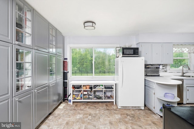 kitchen featuring a sink, freestanding refrigerator, gray cabinets, and black microwave