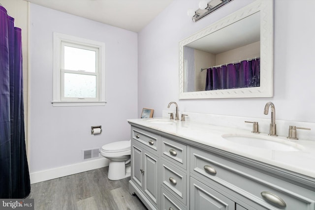 full bathroom with a sink, toilet, double vanity, and wood finished floors