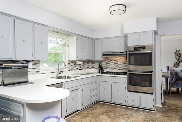 kitchen with gas cooktop, tasteful backsplash, a sink, double oven, and under cabinet range hood