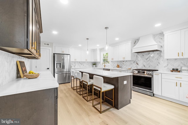 kitchen with a kitchen breakfast bar, a center island, premium range hood, light wood-style floors, and stainless steel appliances