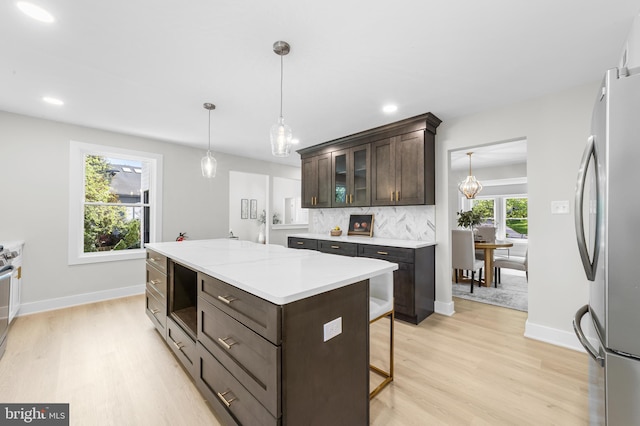 kitchen with dark brown cabinets, light wood finished floors, light countertops, freestanding refrigerator, and decorative backsplash