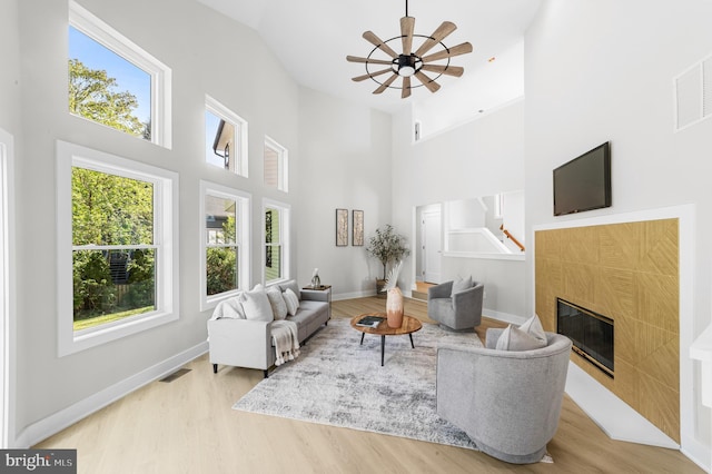 living room with visible vents, wood finished floors, a high ceiling, a tiled fireplace, and a ceiling fan