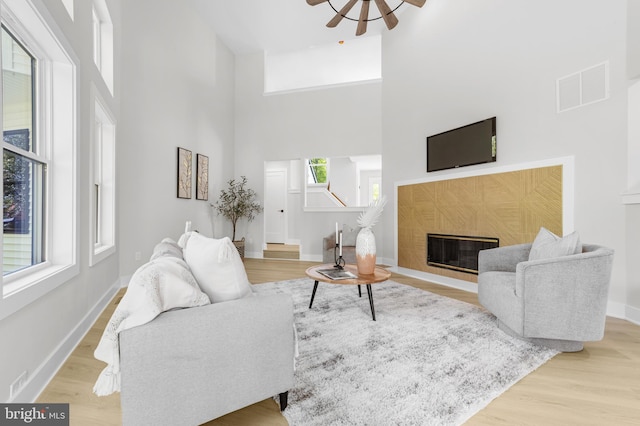 living area with a towering ceiling, ceiling fan, wood finished floors, a tile fireplace, and visible vents