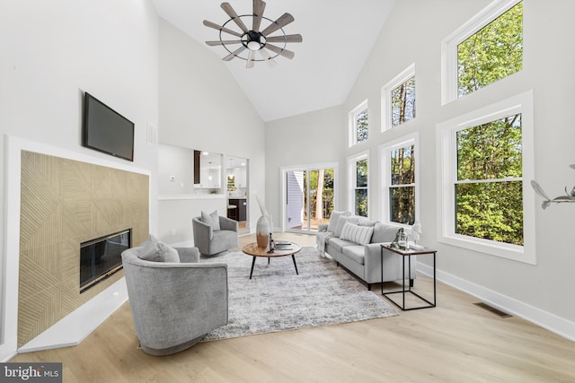living area featuring ceiling fan, visible vents, wood finished floors, a tile fireplace, and high vaulted ceiling