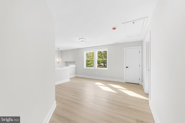 unfurnished living room with baseboards, attic access, and light wood-type flooring