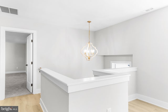 hall featuring visible vents, light wood-style flooring, and an upstairs landing