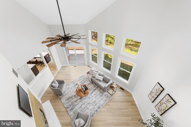 living area with baseboards, a ceiling fan, high vaulted ceiling, and light wood-style flooring