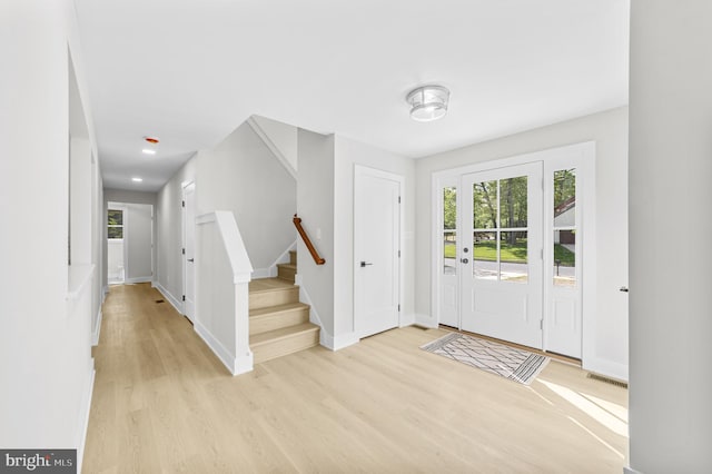foyer entrance featuring light wood-style floors, baseboards, stairway, and visible vents