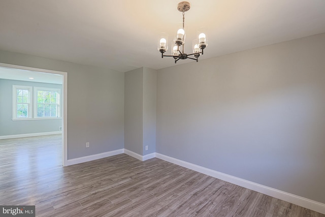 spare room with an inviting chandelier, baseboards, and wood finished floors