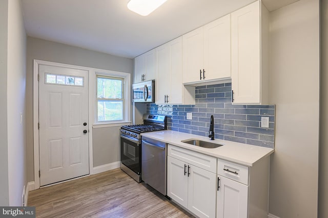 kitchen featuring a sink, light wood finished floors, light countertops, stainless steel appliances, and decorative backsplash