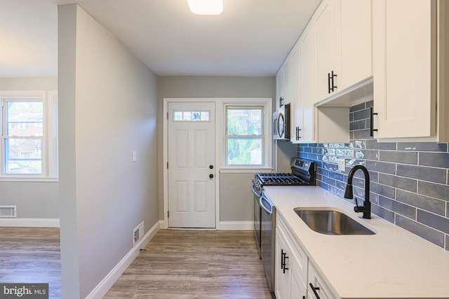 kitchen featuring visible vents, appliances with stainless steel finishes, a sink, baseboards, and white cabinets