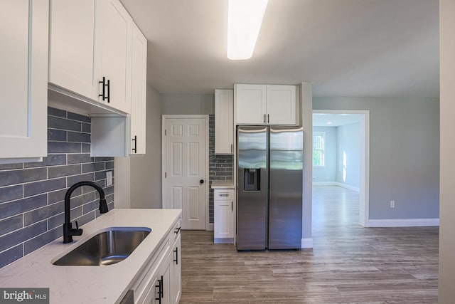 kitchen featuring wood finished floors, light stone countertops, stainless steel refrigerator with ice dispenser, a sink, and backsplash