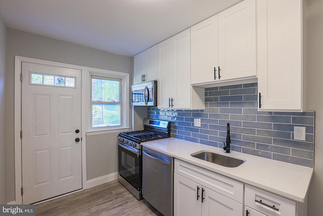 kitchen featuring decorative backsplash, a sink, baseboards, stainless steel appliances, and light wood-style flooring