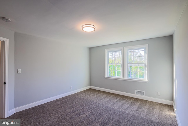 unfurnished room with baseboards, dark colored carpet, and visible vents