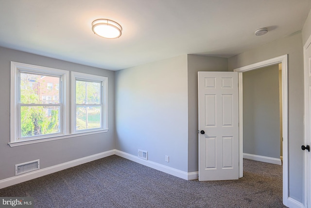 unfurnished bedroom with baseboards, visible vents, and dark colored carpet