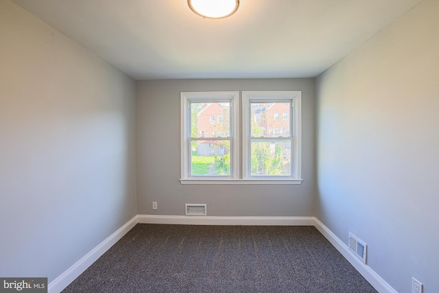 unfurnished room with baseboards, visible vents, and dark carpet