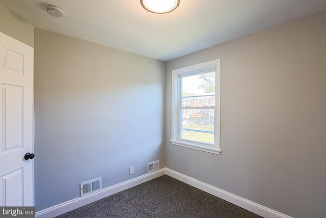 empty room featuring baseboards, dark colored carpet, and visible vents