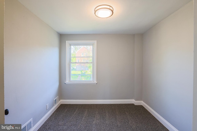 spare room with visible vents, baseboards, and dark carpet