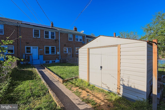 rear view of property featuring a lawn, an outbuilding, brick siding, fence, and a storage unit