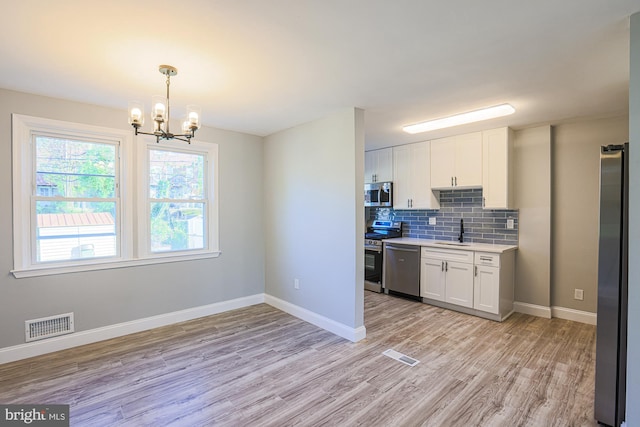 kitchen featuring white cabinets, a notable chandelier, appliances with stainless steel finishes, light countertops, and light wood-style flooring