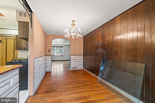 hallway with an inviting chandelier, light wood-style floors, arched walkways, baseboards, and visible vents