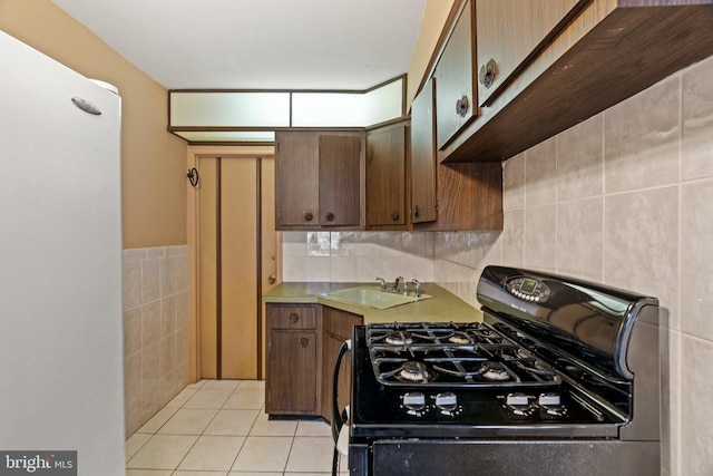 kitchen featuring a sink, gas stove, light countertops, tile walls, and light tile patterned floors