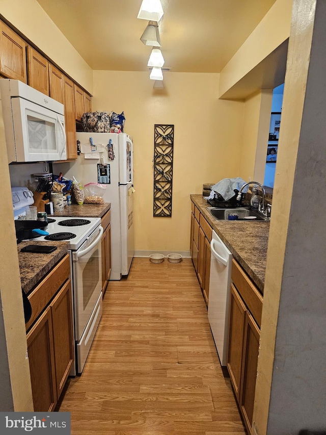 kitchen with dark countertops, brown cabinets, a sink, white appliances, and light wood-style flooring