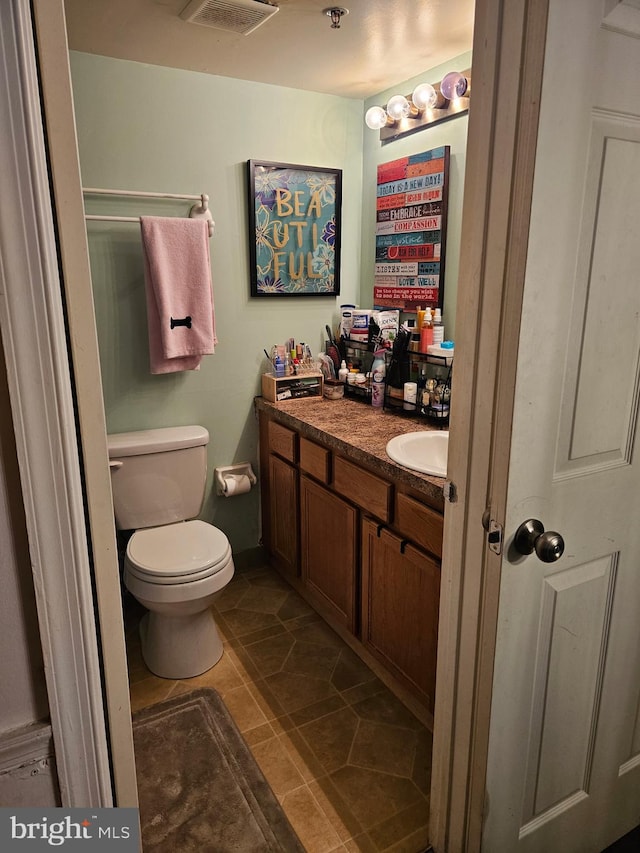 half bath featuring vanity, visible vents, and toilet