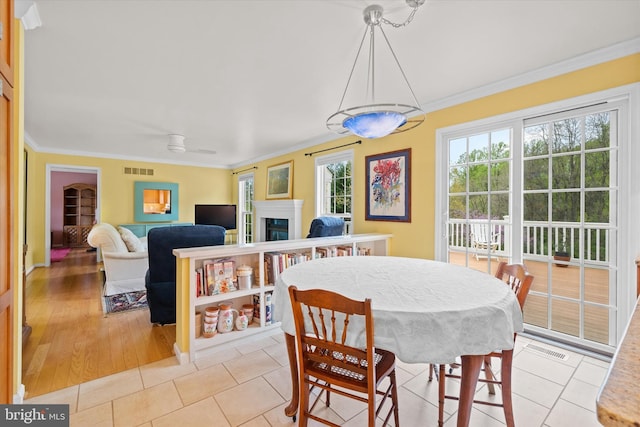 dining area with ornamental molding, visible vents, light tile patterned floors, and a glass covered fireplace