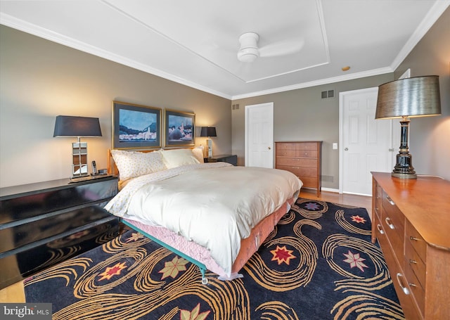 bedroom featuring wood finished floors, visible vents, crown molding, and a tray ceiling
