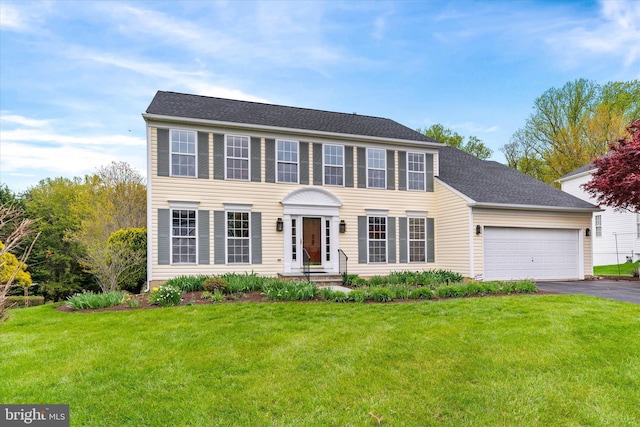 colonial home featuring roof with shingles, aphalt driveway, a front lawn, and a garage