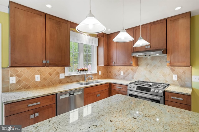 kitchen with hanging light fixtures, light stone counters, under cabinet range hood, appliances with stainless steel finishes, and a sink