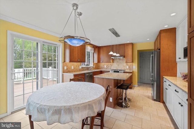 kitchen with stainless steel appliances, under cabinet range hood, a kitchen island, backsplash, and a kitchen breakfast bar