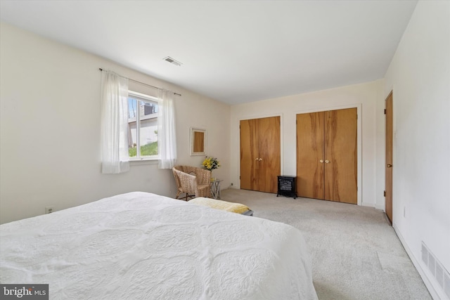bedroom with multiple closets, visible vents, and light carpet