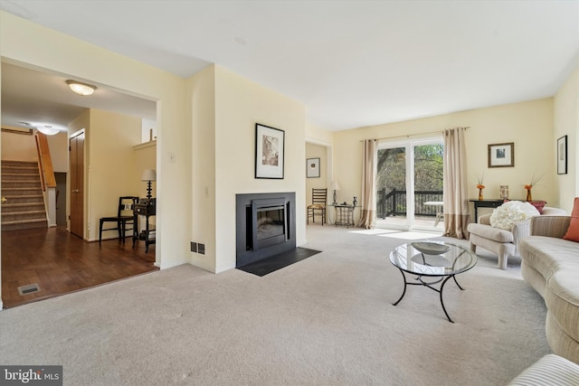 living area with visible vents, carpet flooring, a fireplace with flush hearth, and stairway