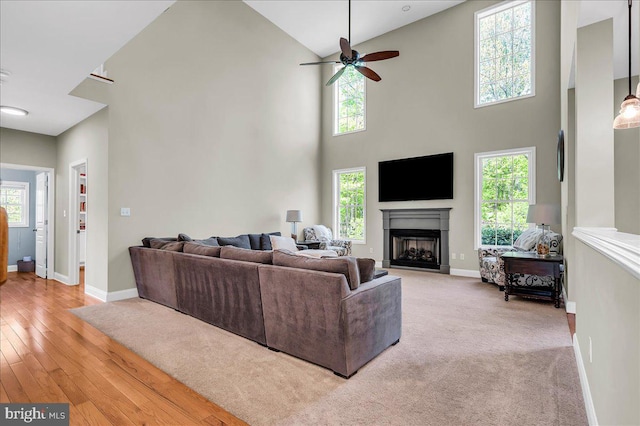 living area with a towering ceiling, wood finished floors, a fireplace, baseboards, and ceiling fan