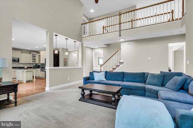 living room featuring visible vents, a towering ceiling, light carpet, baseboards, and stairway