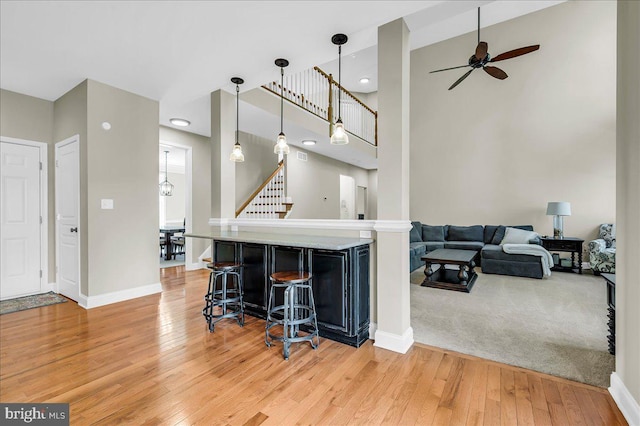 kitchen with ceiling fan, a breakfast bar, light wood-style floors, decorative light fixtures, and baseboards