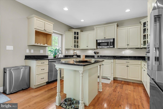 kitchen featuring a kitchen island, appliances with stainless steel finishes, glass insert cabinets, and light wood-style flooring