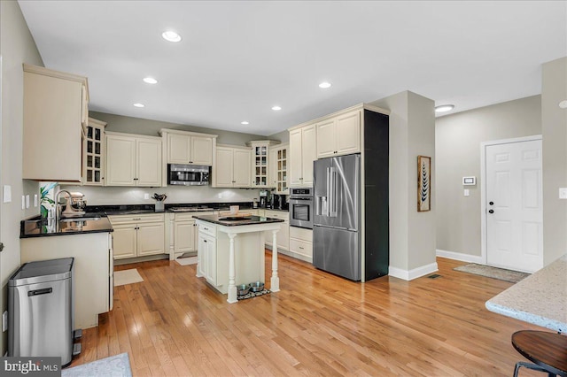 kitchen with appliances with stainless steel finishes, glass insert cabinets, a sink, and light wood-style floors