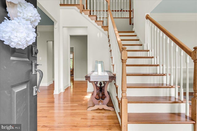 stairs with crown molding, baseboards, a high ceiling, and wood finished floors