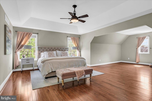 bedroom featuring baseboards, multiple windows, a tray ceiling, and hardwood / wood-style floors
