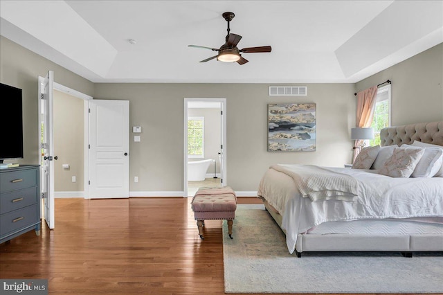 bedroom with visible vents, a raised ceiling, wood finished floors, and multiple windows