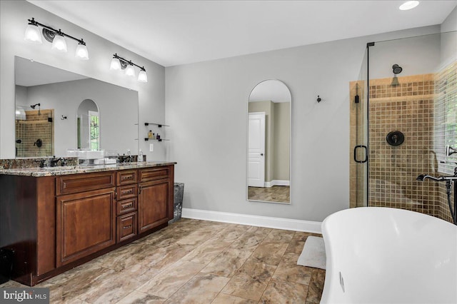 bathroom featuring double vanity, a freestanding bath, a stall shower, a sink, and baseboards