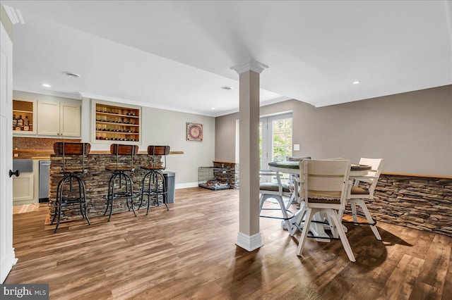 dining space featuring a dry bar, wood finished floors, baseboards, ornate columns, and recessed lighting
