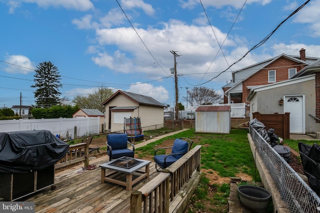 view of yard with a fire pit, a deck, a fenced backyard, a storage unit, and an outbuilding