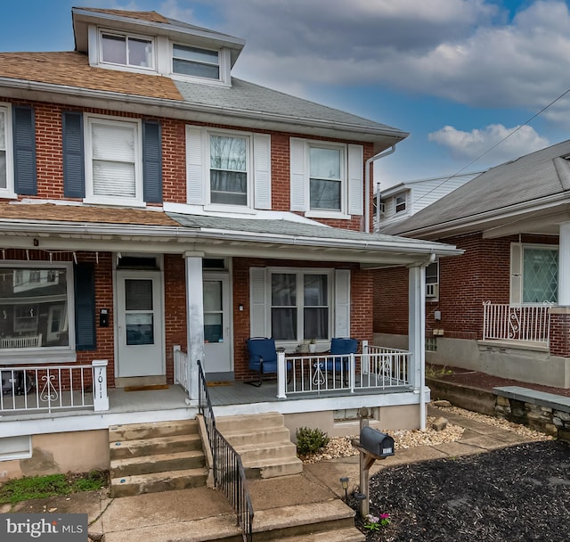 multi unit property featuring roof with shingles, covered porch, and brick siding